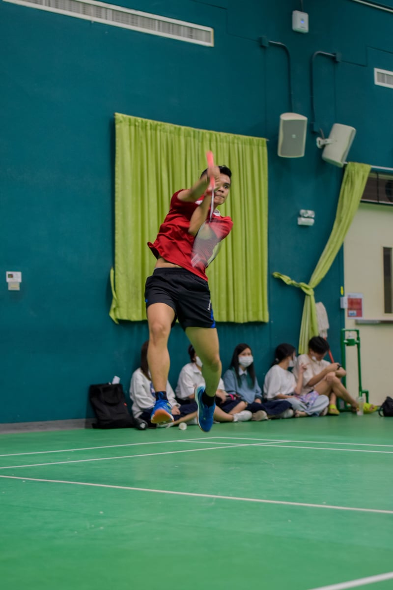 Palm jumping for a badminton smash in a red jersey.